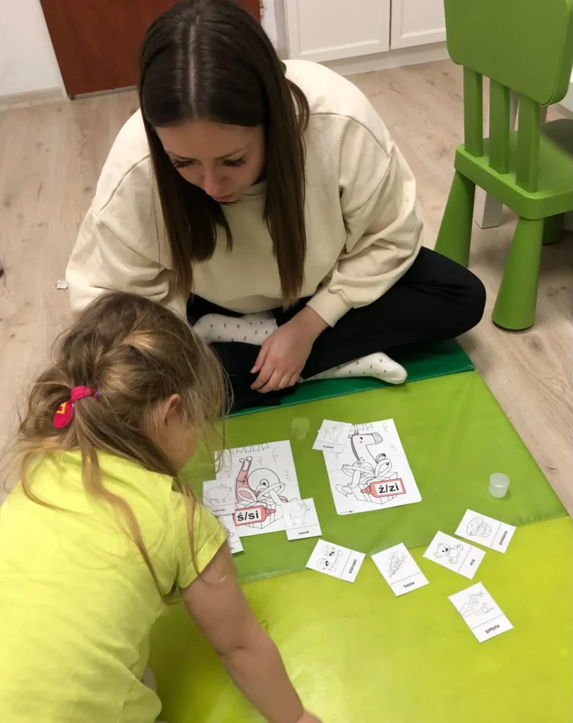 Zajęcia logopedyczne – dziewczynka ćwiczy z logopedką na macie